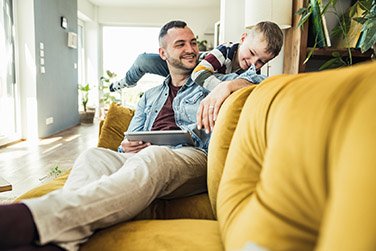 Dad sitting on yellow sofa with son playing in living room at home