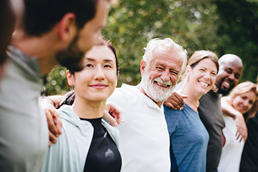 Diverse people standing outdoors in a line with their arms around each other's shoulders smiling