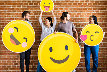 Men and women holding positive emoticons in front of a brick wall